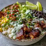 A finished Carnitas Burrito Bowl topped with zesty salsa and creamy lime crema, served fresh on a rustic table.