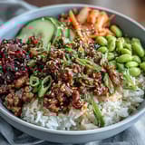 A vibrant Korean ground beef bowl with spicy gochujang beef, fresh vegetables, kimchi, and sesame seeds over steaming rice.