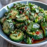 Thinly sliced cucumbers in a light sesame-rice vinegar dressing, topped with toasted sesame seeds and red pepper flakes for a crisp, vibrant appetizer.