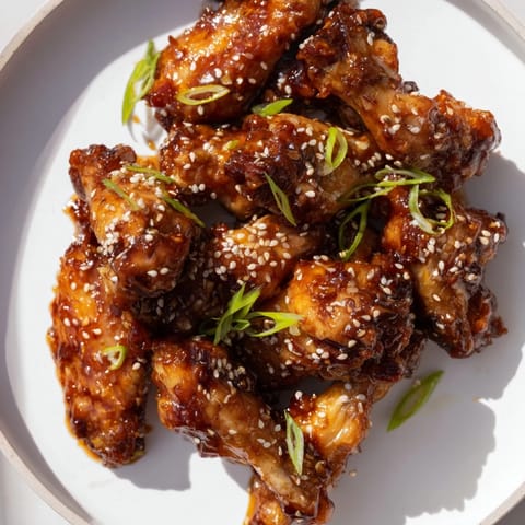 Close-up of perfectly caramelized Asian Sticky Wings, sticky and savory, scattered with sesame seeds.
