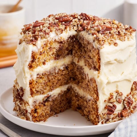 Moist Hummingbird Cake, frosted generously, with sliced banana and pecan garnish on a plate.