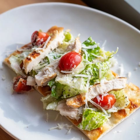 Sliced grilled chicken on crispy flatbread topped with Caesar salad, Parmesan, and cherry tomatoes.
