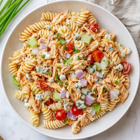 A chilled rotini pasta salad featuring shredded buffalo chicken, crisp veggies, and blue cheese crumbles, perfect for summer picnics.