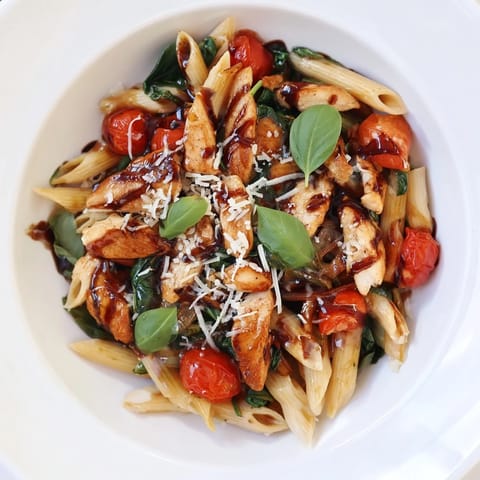 A close-up view of sautéed chicken coated in a rich balsamic sauce, tossed with pasta, garlic, and wilted greens for a vibrant dinner.