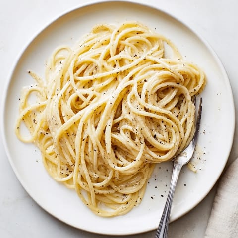 This image shows a warm skillet of Spaghetti Cacio e Pepe, glistening with a silky, peppery cheese sauce.