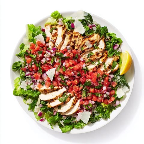 Sliced grilled chicken sits on a bed of mixed greens, topped with a fresh tomato-basil bruschetta topping and shaved Parmesan.