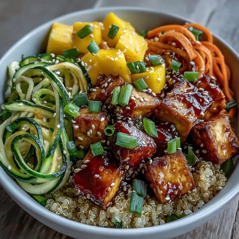 Golden crispy baked tofu sits atop fluffy quinoa with spiralized zucchini, carrots, and fresh mango slices in a vibrant bowl.