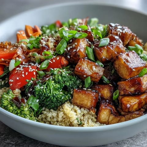 Golden crispy tofu and vibrant stir-fried vegetables on a bed of fluffy quinoa, all coated in glossy teriyaki sauce.