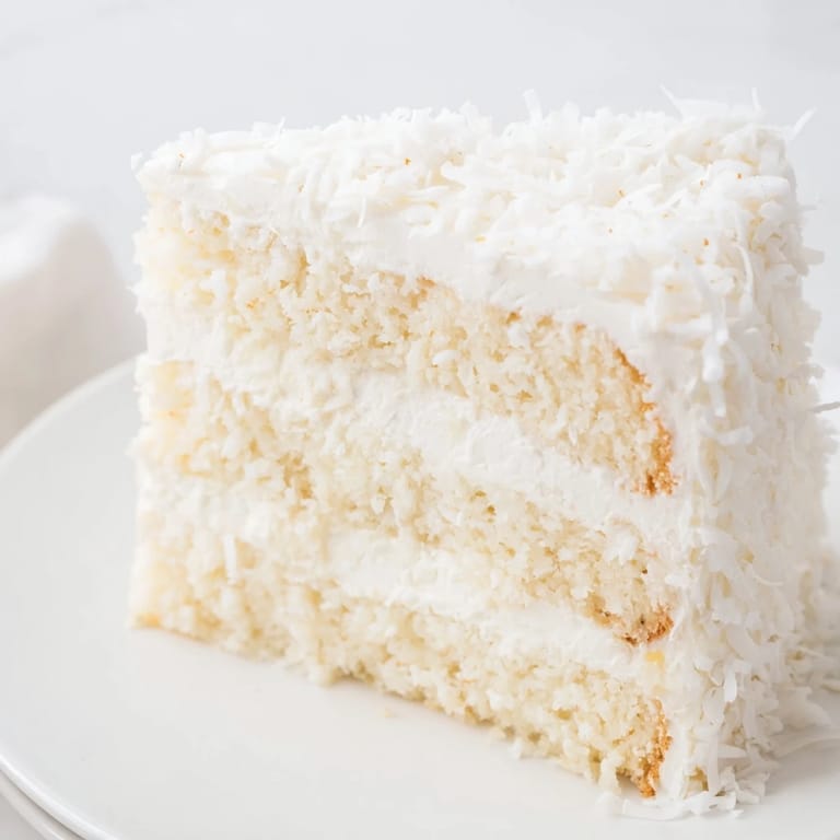 This homemade coconut cake showcases fluffy white layers with a billowy seven-minute meringue, ready to serve.