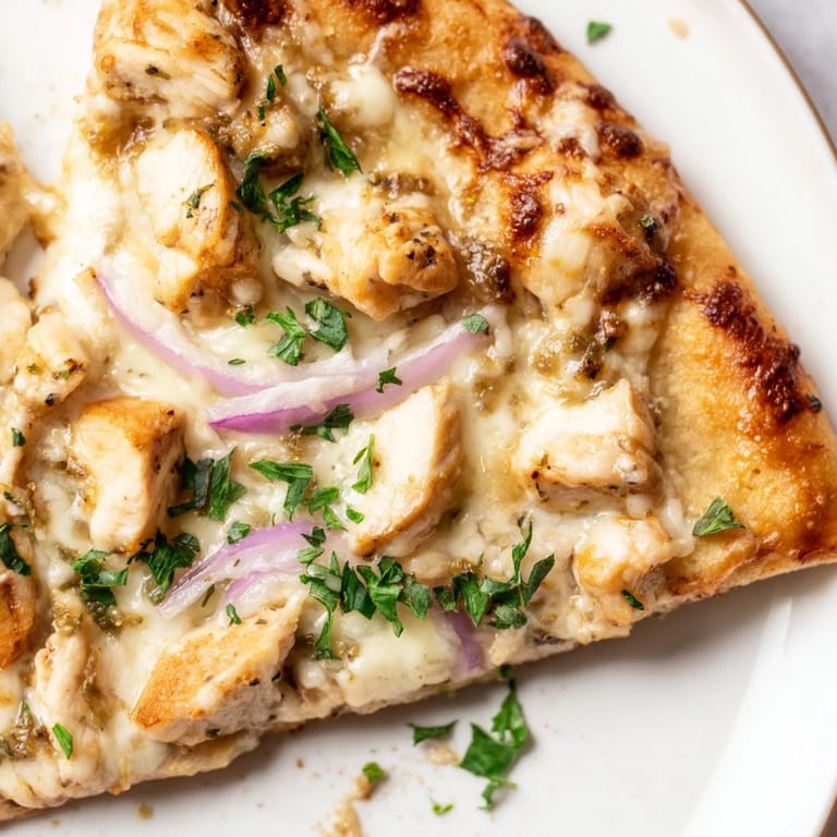 Fresh parsley sprinkles over a bubbling Chicken Alfredo Pizza, with creamy sauce, chicken, and cheese glistening in warm light.