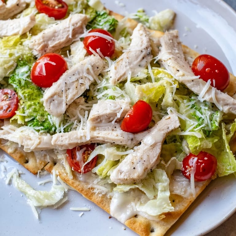 A close-up of Caesar Chicken Flatbread garnished with Parmesan shavings and lemon wedges for serving.