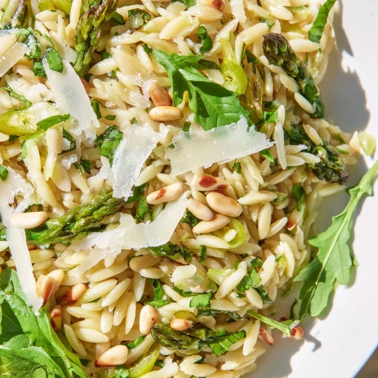 A vibrant spring salad bowl showcases the Asparagus Lemon Orzo Salad, with shaved greens, zesty lemon wedges, and golden pine nuts for crunch.