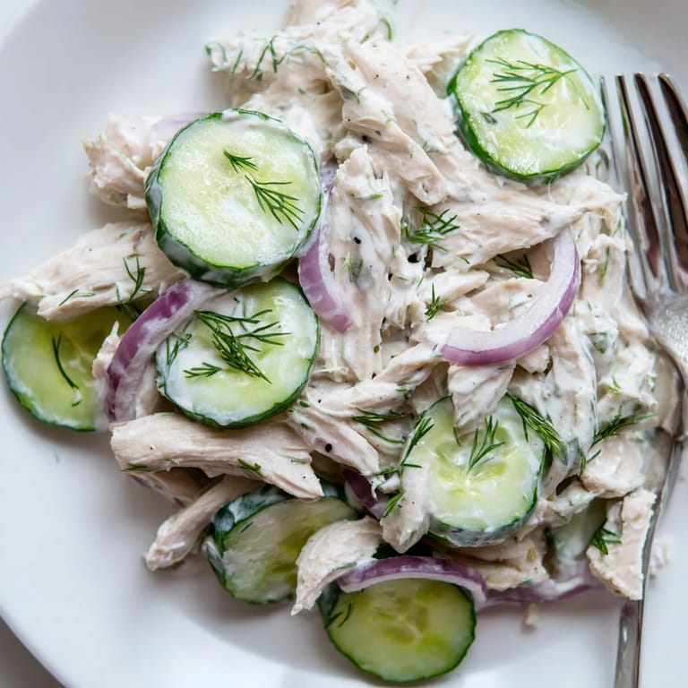 A close-up of creamy cucumber chicken salad with Greek yogurt dressing, diced chicken, and thinly sliced cucumbers on a wooden table.