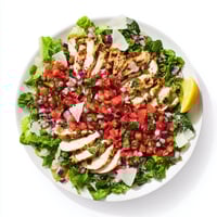 Sliced grilled chicken sits on a bed of mixed greens, topped with a fresh tomato-basil bruschetta topping and shaved Parmesan.