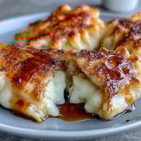 Golden brown pan-fried Chīzu Imomochi dumplings with a sticky soy-honey glaze are served warm on a white plate.